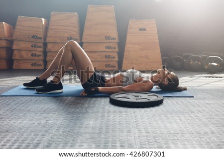Side view shot of fitness woman resting on exercise mat with a heavy weight plate on floor. Female athlete lying on her back after a gym workout