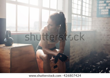 Young woman sitting on a box at gym after her workout. Female athlete taking rest after exercising at gym.