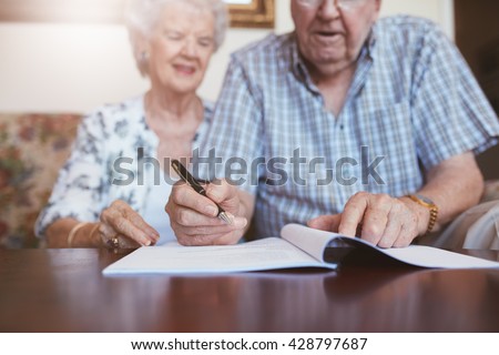 Senior couple signing will documents. Elderly caucasian man and woman sitting at home and signing some paperwork, focus on hands.