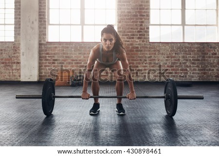 Female performing deadlift exercise with weight bar. Confident young woman doing weight lifting workout at gym.