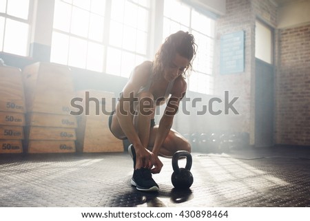 Fit young woman at gym tying her shoelace. Muscular female model getting ready for kettle bell workout.