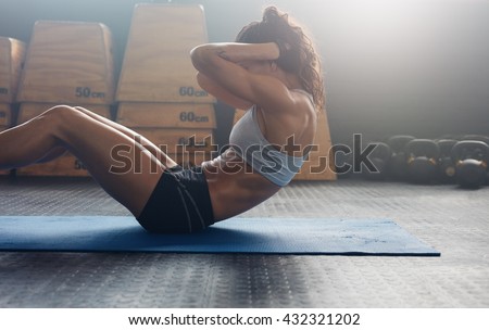 Sporty young female athlete on yoga mat doing situps in gym. Fitness woman doing abs crunches.