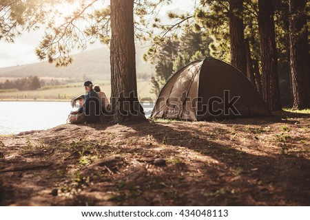 Portrait of senior couple camping by a lake. Man and woman sitting under a tree looking away a the lake on summer day.