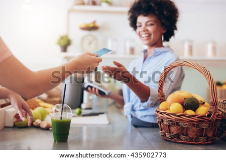 Shot of a female juice bar owner taking payment from customer. Female customer paying for juice with credit card.