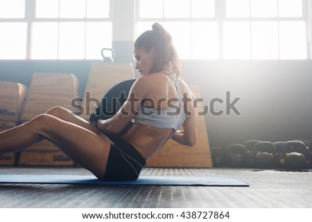 Woman doing sit ups with holding a weight plate. Fitness woman working out on core muscles at cross fit gym.