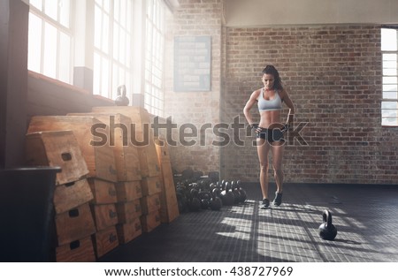 Full length image of fit young woman walking in the crossfit gym. Female athlete preparing herself before a intense training.