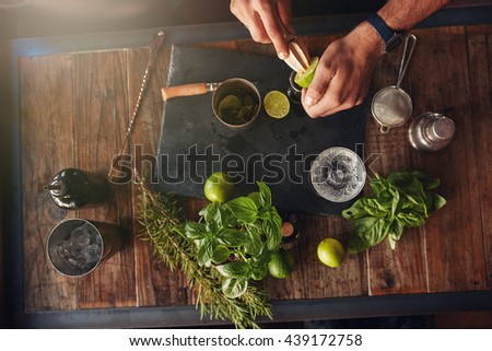 Bartender hands juicing lemon with a reamer. Bartender experimenting with creating new cocktails ideas. Cocktail accessories with lemons, basil and lavender on table.