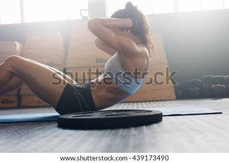 Side view of fit young woman doing pilates, working on abdominal muscles. Fitness woman exercising to improve core muscle strength in gym.