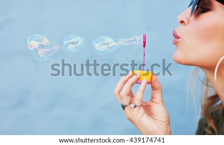 Close up side view shot of young female model blowing soap bubbles on blue background. Focus on hands and wand.