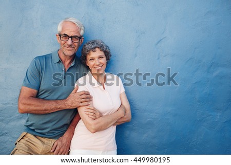 Portrait of happy mature couple standing together against blue wall. Middle aged man and woman looking at camera and smiling on blue background