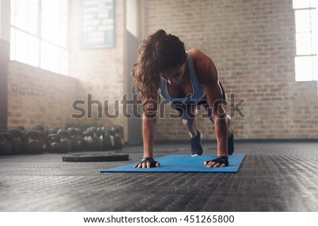 Young muscular woman doing core exercise on fitness mat in the gym. Fit female doing press-ups during the training in the health club.