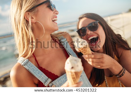 Two best friends having ice cream together outdoors. Close up of young women eating ice cream and laughing.