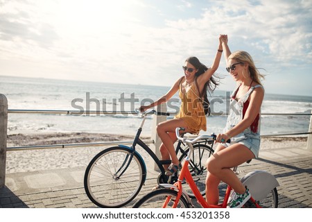 Female friends enjoying cycling on a summer day. Two young female friends riding their bicycles on the seaside promenade.