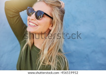 Cheerful young woman in sunglasses against blue background. Beautiful female model with long hair.