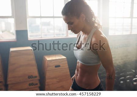 Side view of strong woman standing in the gym. Fitness female taking a break from intense workout.