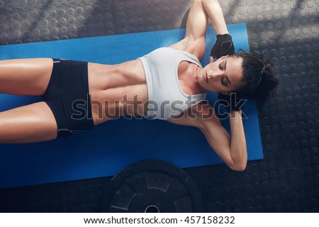 Top view of woman exercising on yoga mat. Fitness female lying on exercise mat with her hands behind head at gym.