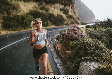 Fitness woman running on highway around the mountains. Female athlete training outdoors during rain.