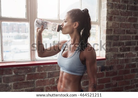 Fit young woman drinking water in the gym. Muscular woman taking break after exercise.