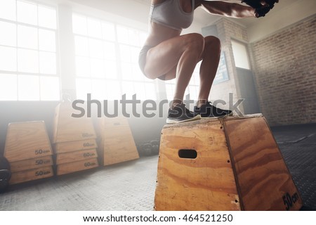 Fit young woman box jumping at a crossfit gym. Female athlete is performing box jumps at gym, with focus on legs.