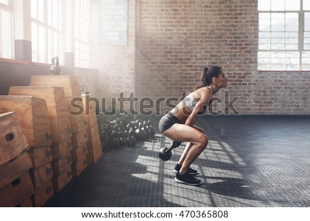 Side view of tough young woman exercising with kettle bell at gym. Fit female athlete doing crossfit workout at gym.