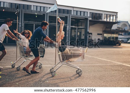 Young friends having fun on a shopping trolley. Multiethnic young people racing on shopping cart.