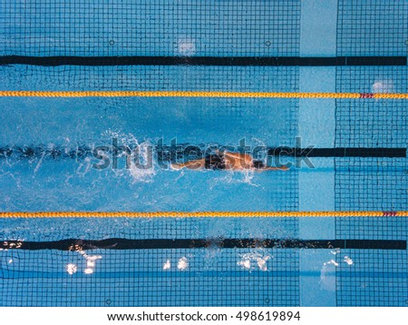 Top view shot of young man swimming laps in a swimming pool. Male swimmer swimming the front crawl in a pool.