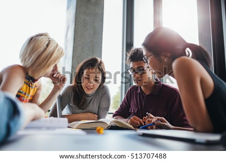 University students in cooperation with their assignment at library. Group of young people sitting at table reading books.