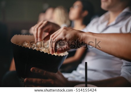 Close up shot of young people eating popcorn in movie theater, focus on hands.