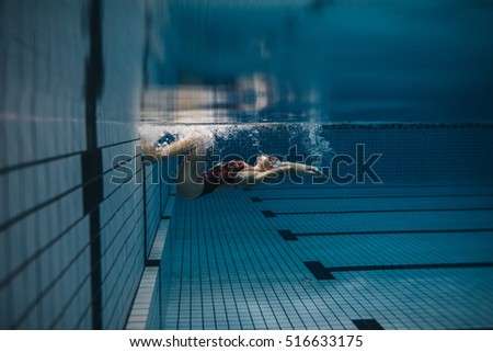 Shot of fit young woman turning over underwater. Female swimmer in action inside swimming pool.