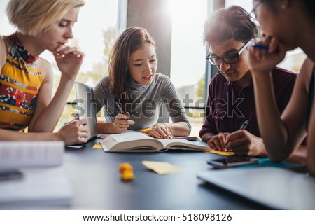 Multiethnic young people sitting at table reading reference books for study notes. Group of young students doing school assignment in library.
