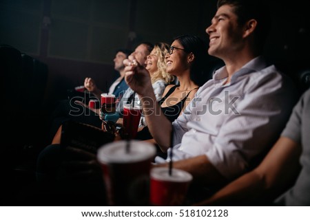 Group of people in theater with popcorn and drinks. Young friends watching movie in cinema.