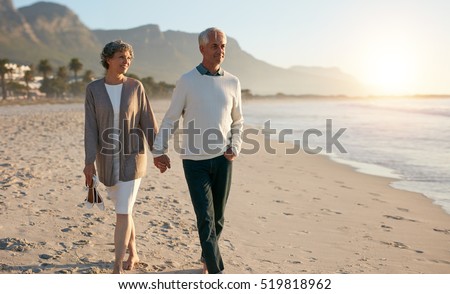 Shot of senior couple walking along beach together holding hands.