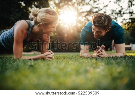 Fit young man and woman exercising in park. Smiling caucasian couple doing core workout on grass.
