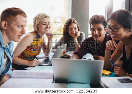 Multiracial group of young students studying in the library. Young people sitting together at table with books and laptop for researching information for their project.