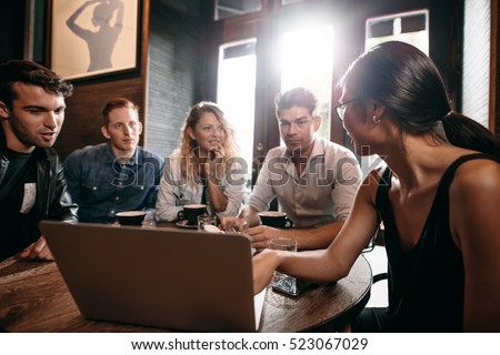 Smiling friends spending their time in coffee shop and discussing something while looking at laptop. Woman showing something to her friends sitting at cafe table.