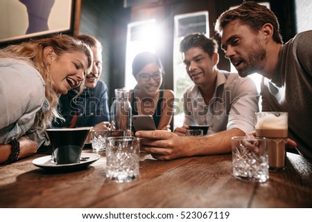 Young friends looking at smart phone while sitting in cafe. Mixed race people sitting at a table in restaurant using mobile phone.