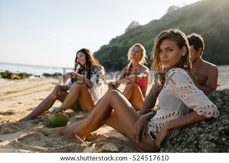 Beautiful young woman relaxing on the beach with her friends in background. Group of friends on beach holiday.