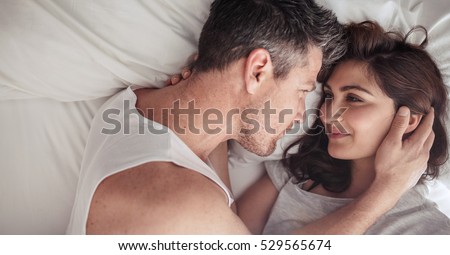 Overhead close up of young couple lying in bed together. Romantic couple in love looking at each other.