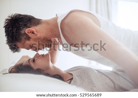 Side view shot of romantic couple during foreplay in bed. Intimate young man and woman in bedroom.