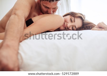 Beautiful couple being romantic and passionate in bed. Man and woman together in bed. He is kissing her.