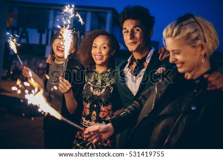 Shot of young friends at night with fireworks enjoying party. Group of friends with sparklers on road in evening.