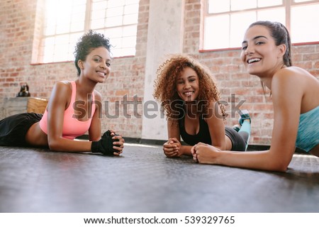Portrait of three young women in fitness class looking at camera and smiling. Female friends exercising together in fitness class.
