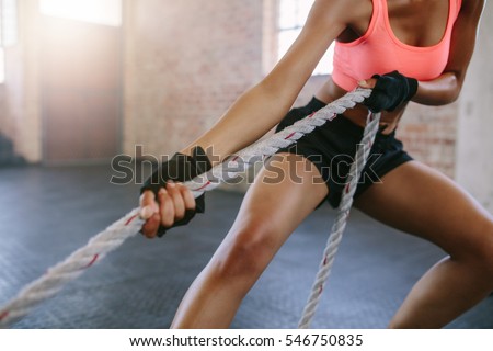 Cropped shot of strong young woman pulling rope at a gym. Female working out with rope at gym.