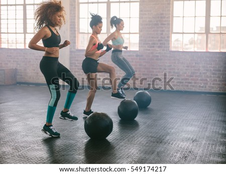 Young women exercising in aerobics class with medicine balls on floor. Three females doing workout together in gym.