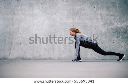 Full length shot of fit young woman doing stretching workout. Fitness model exercising in morning outdoors.