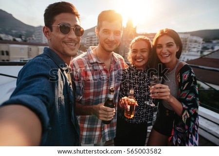 Young friends partying together taking selfie. Group of people with drinks on a rooftop party taking selfie.
