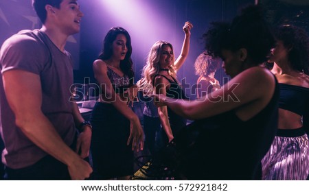 Group of friends dancing in club. Young men and women having fun at disco  nightclub.