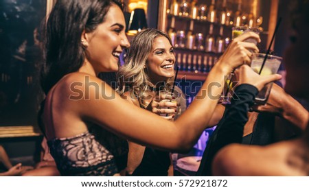 Group of young people celebrating at pub. Friends toasting cocktails in night club.