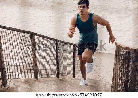 Fitness man running up the steps on beach. Muscular young male runner working out on steps on sea shore.