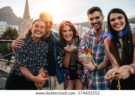 Group of friends hanging out together on rooftop party. Young people enjoying at party with confetti.